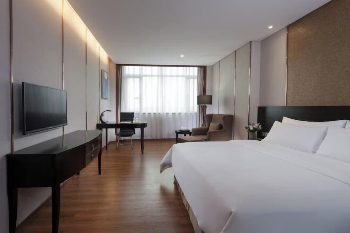 A hotel room with a bed, a desk, a chair, a television, and a window with curtains.