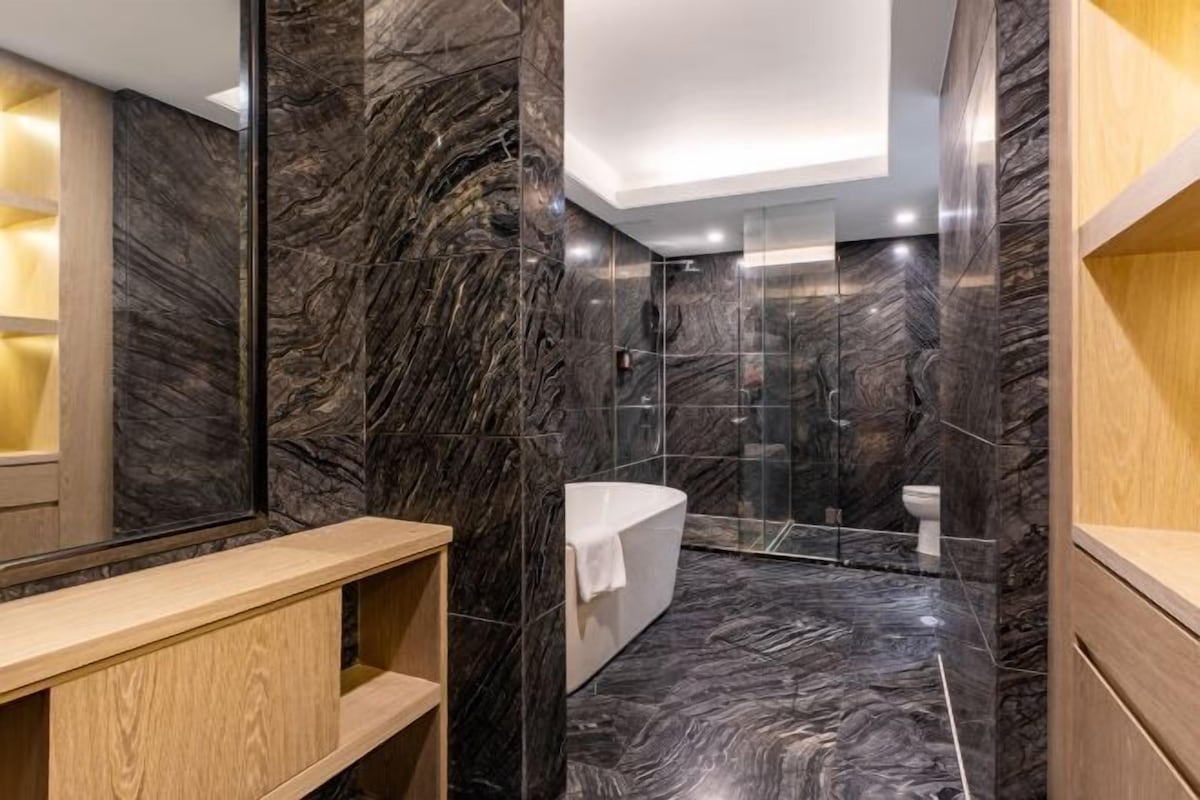 A modern bathroom with a marble floor, a white bathtub, and a glass shower enclosure.
