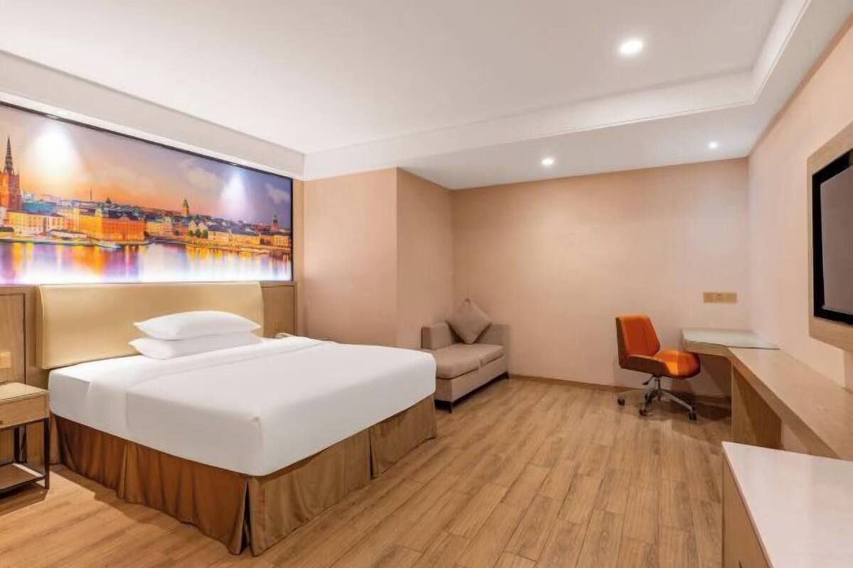 A hotel room with a bed, a desk, a chair, and a large painting of a cityscape.