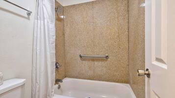 A bathroom with a bathtub, a shower curtain, a towel rack, and a door with a handle.