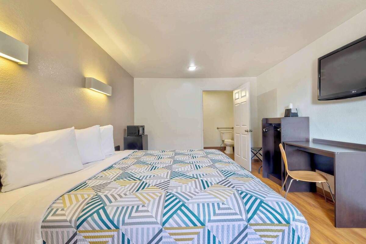 Ett hotellrum med en stor säng, ett skrivbord med en stol, en tv som är monterad på väggen och ett badrum som syns genom en öppen dörr.