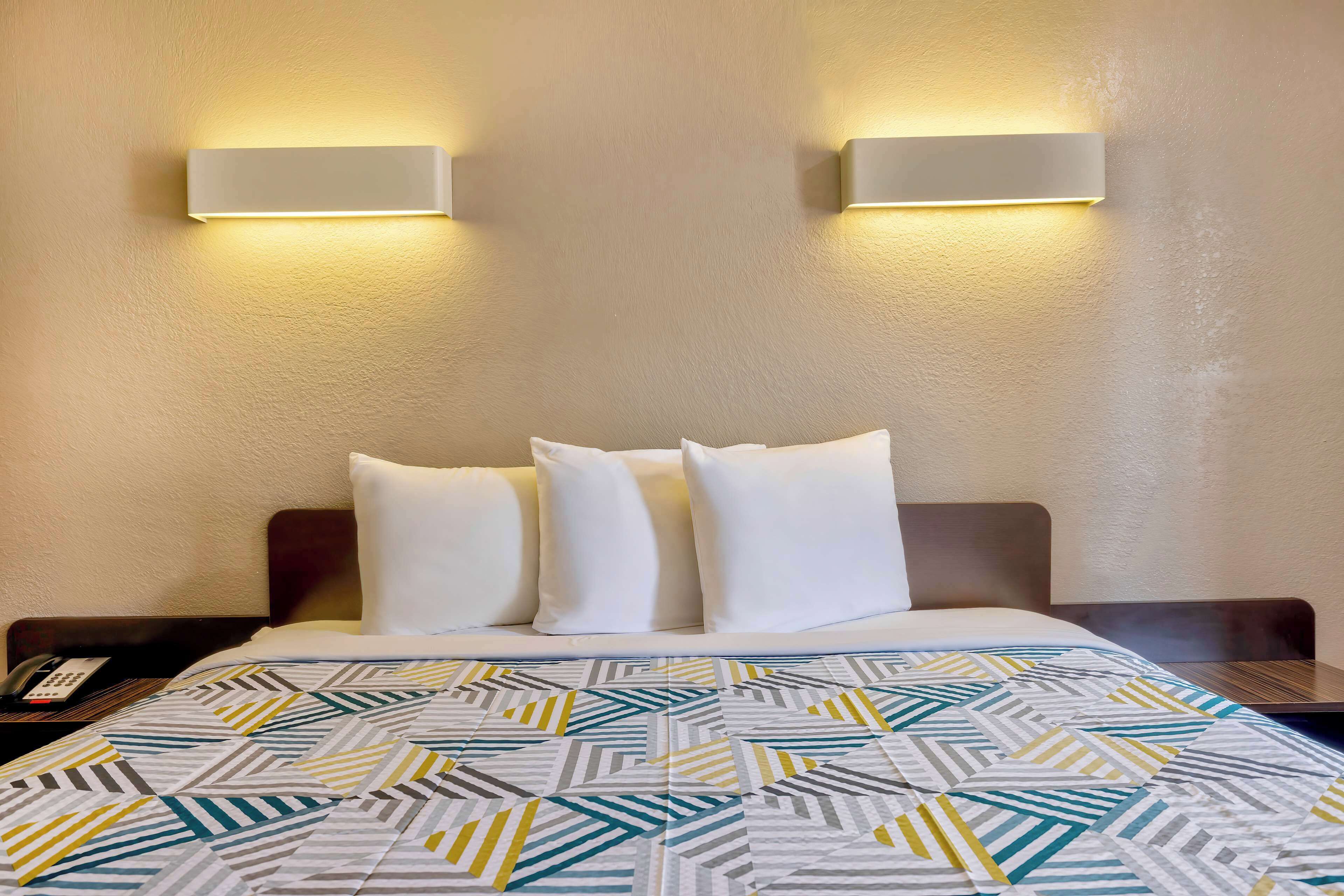 Ein Hotelzimmer mit einem ordentlich bezogenen Bett, einer gemusterten Tagesdecke und zwei Wandleuchten.