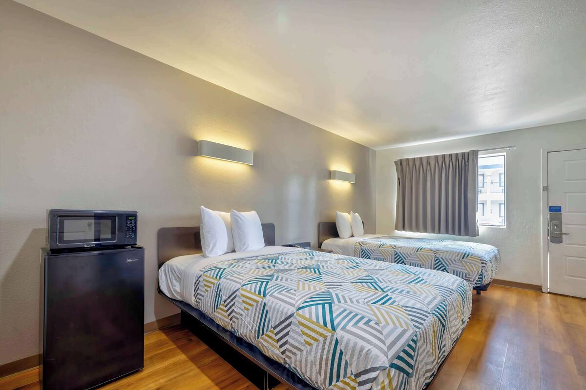 Ett hotellrum med två sängar, en mikrovågsugn och en dörr med ett fönster.