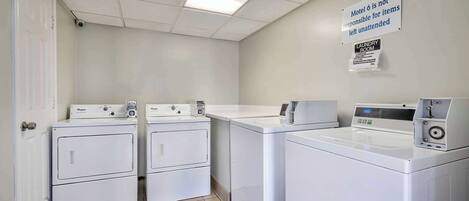 A laundry room with two front-loading washers and a front-loading dryer, a sign indicating the room is not responsible for unattended items, and a laundry room sign.