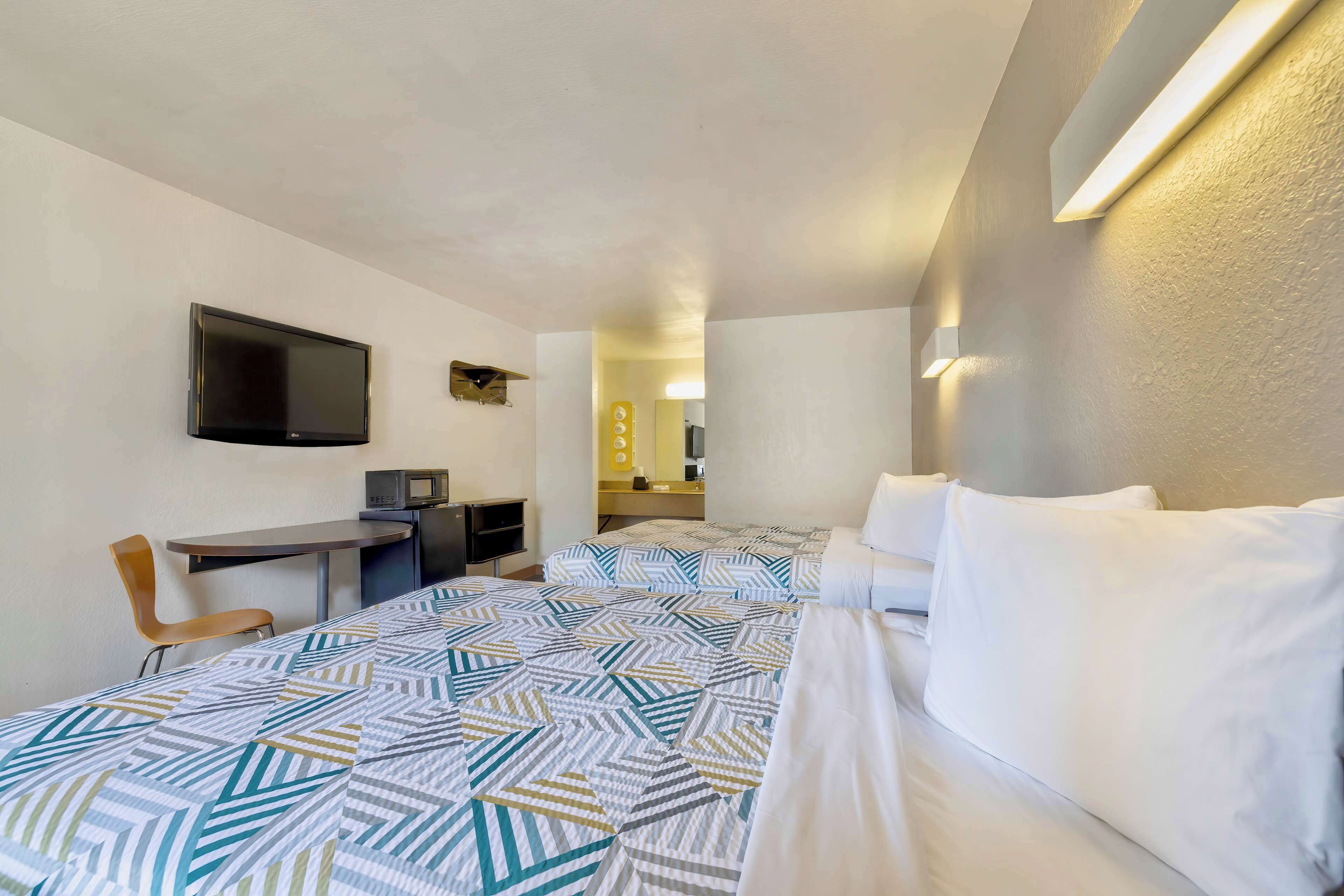 Une chambre d’hôtel avec deux lits, un bureau avec une chaise, une télévision et un four à micro-ondes.