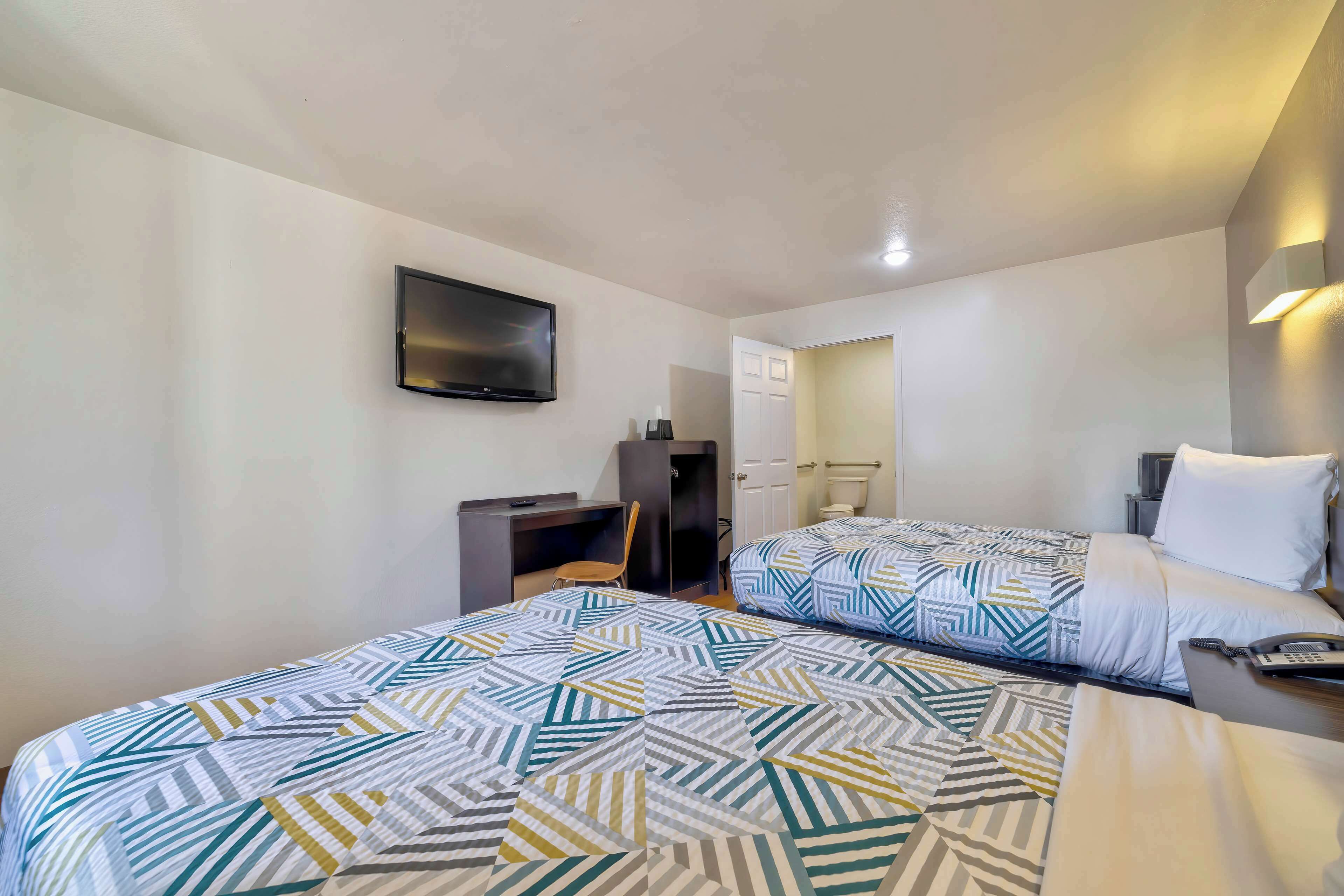 A hotel room with two beds, a desk, a chair, a TV mounted on the wall, and a bathroom door.