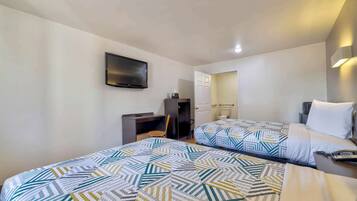 A hotel room with two beds, a desk, a chair, a TV mounted on the wall, and a bathroom door.
