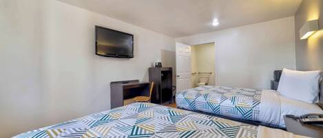 A hotel room with two beds, a desk, a chair, a TV mounted on the wall, and a bathroom door.