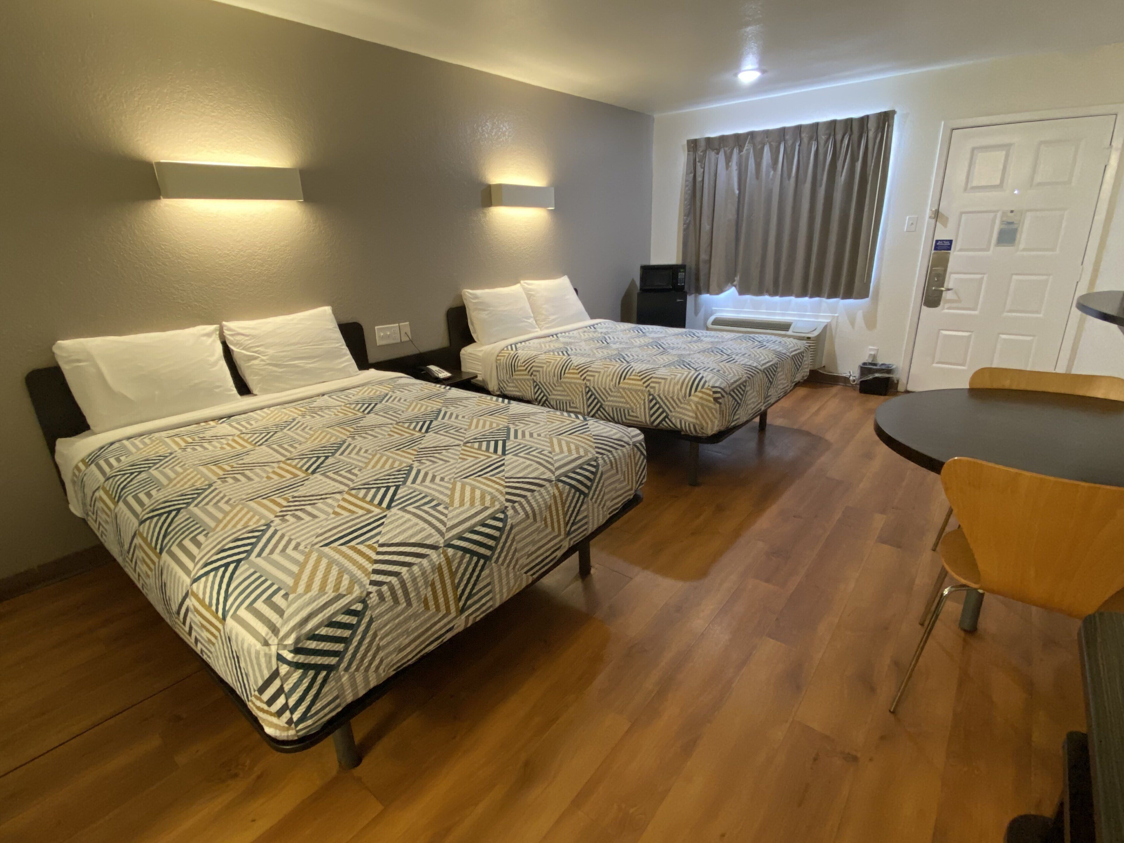 A hotel room with two beds, a dining table, and a window with curtains.