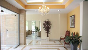 A spacious lobby with a chandelier, potted plants, and a large mirror. - Hotel Giorgio (Acharnes)