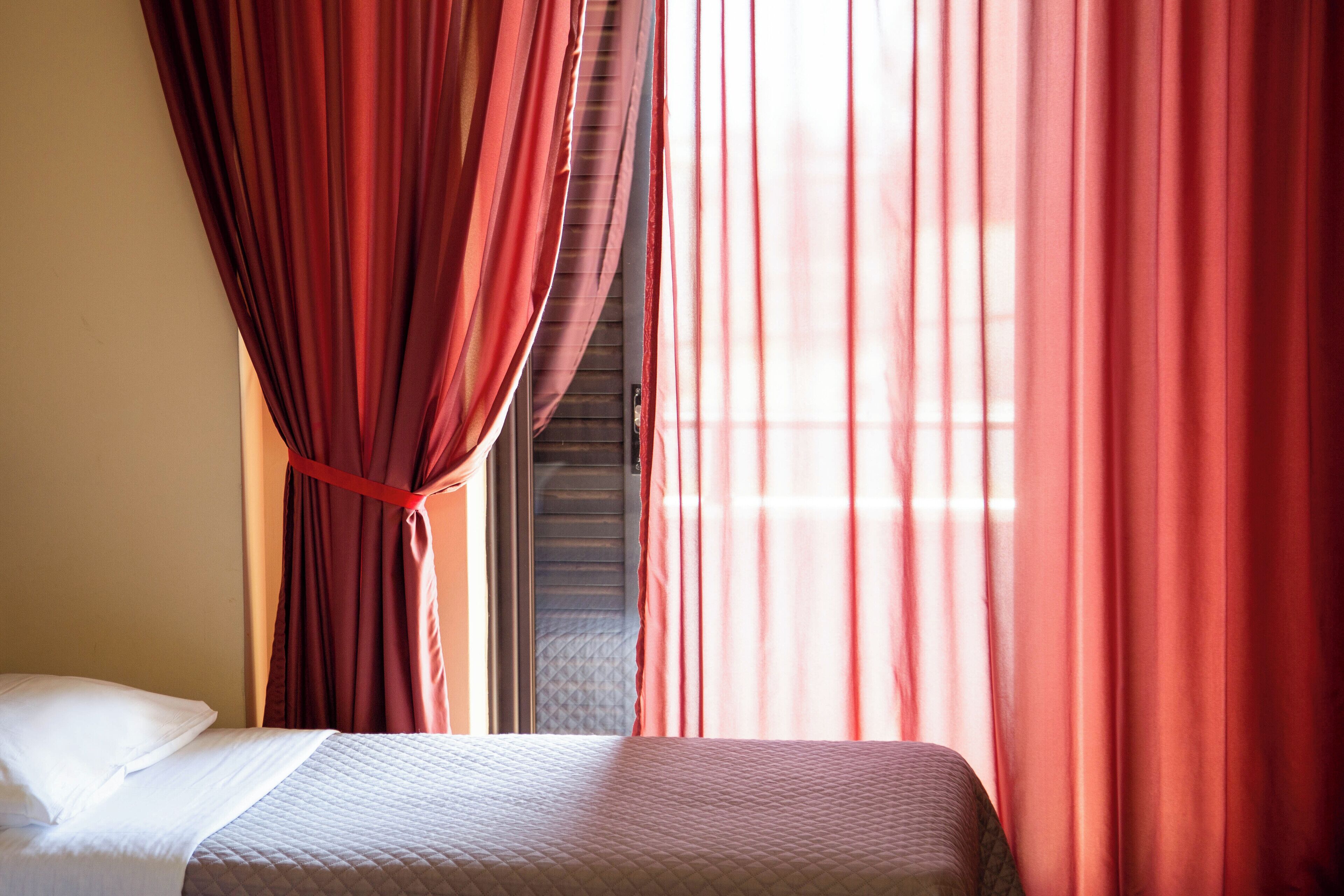 A hotel room with a bed, red curtains, and a window.