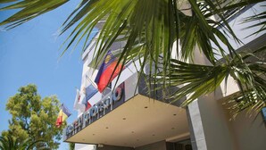 A hotel entrance with a modern facade, flags, and palm trees. - Hotel Giorgio (Acharnes)
