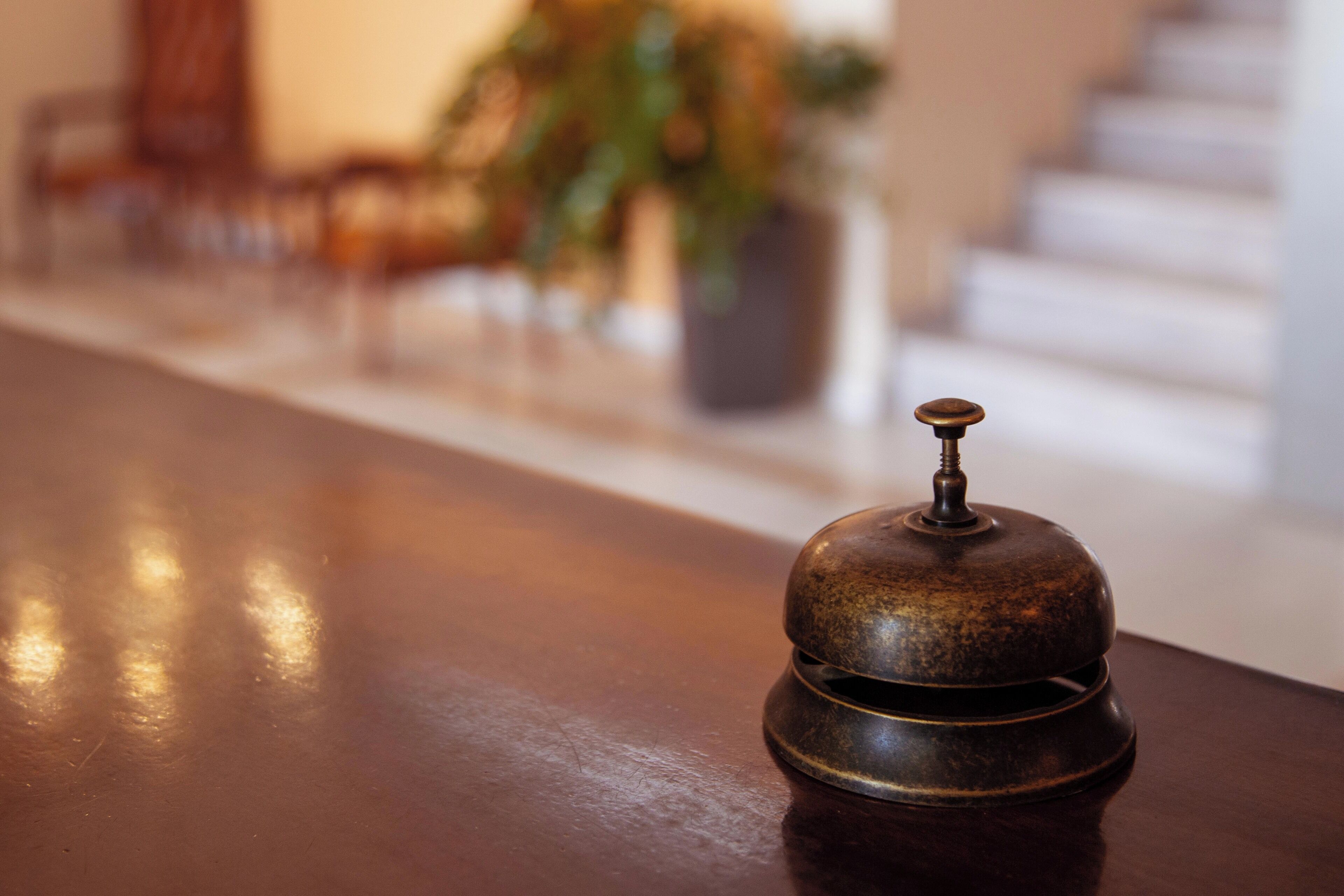 A brass bell on a wooden table in a hotel lobby.