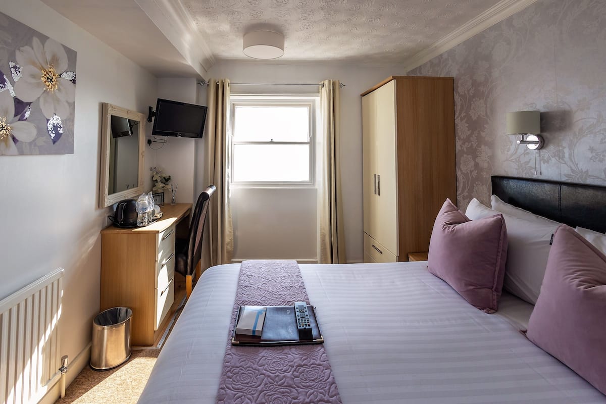 Habitación de hotel con cama, escritorio con silla, televisión, ventana con cortinas y armario.