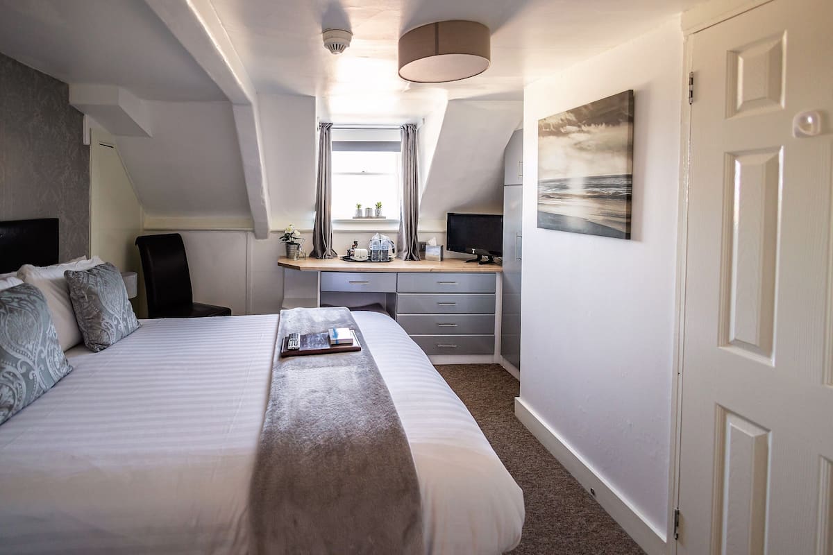 Un dormitorio con una cama grande, un escritorio y un ventanal con cortinas.