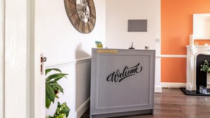 En reception med et 'Welcome'-skilt, et ur og en pejs i baggrunden.