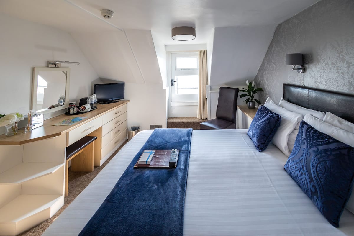 Una habitación de hotel moderna con una cama grande, un escritorio con una computadora portátil, un televisor y una planta en maceta.
