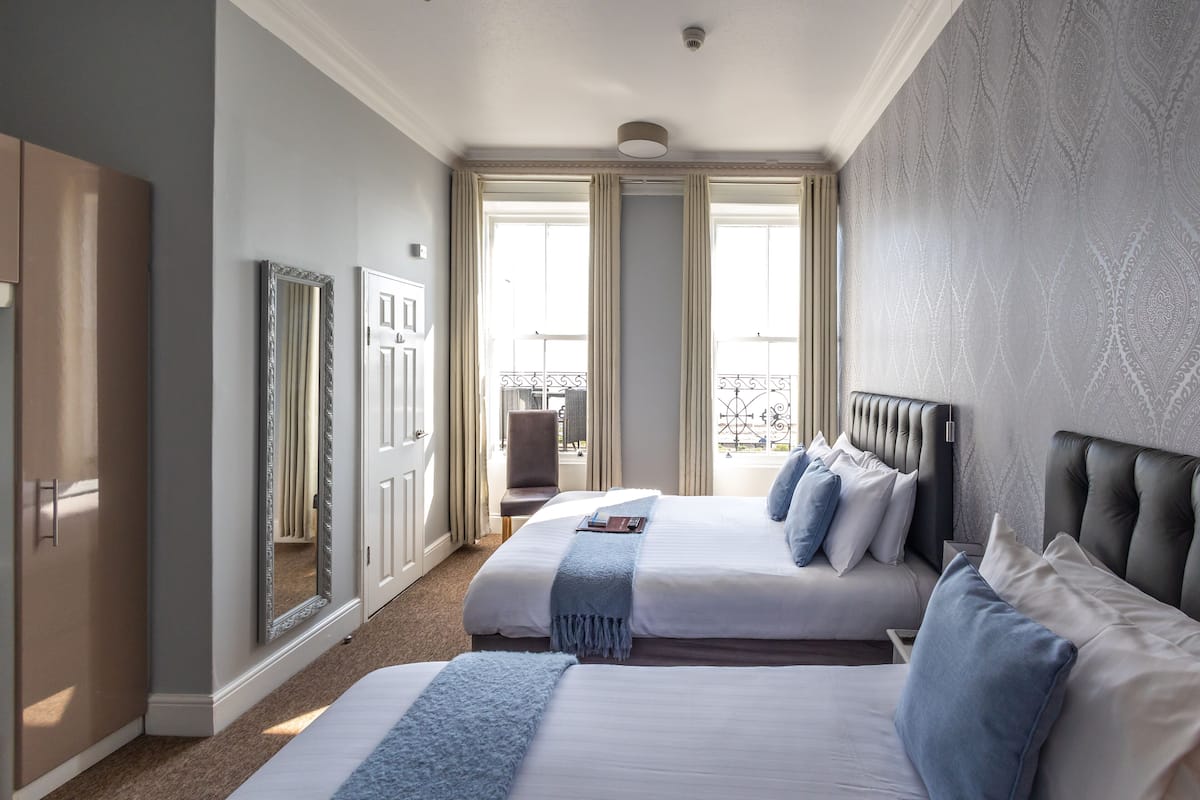 Una habitación de hotel con dos camas, un espejo grande y vistas al exterior a través de una ventana.