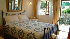A bedroom with a bed, a nightstand, a window with curtains, and a view of the outdoors. - The Cottage Marsh B&B (Honiton)