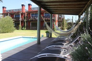 A poolside area with lounge chairs and a hammock under a wooden pergola.