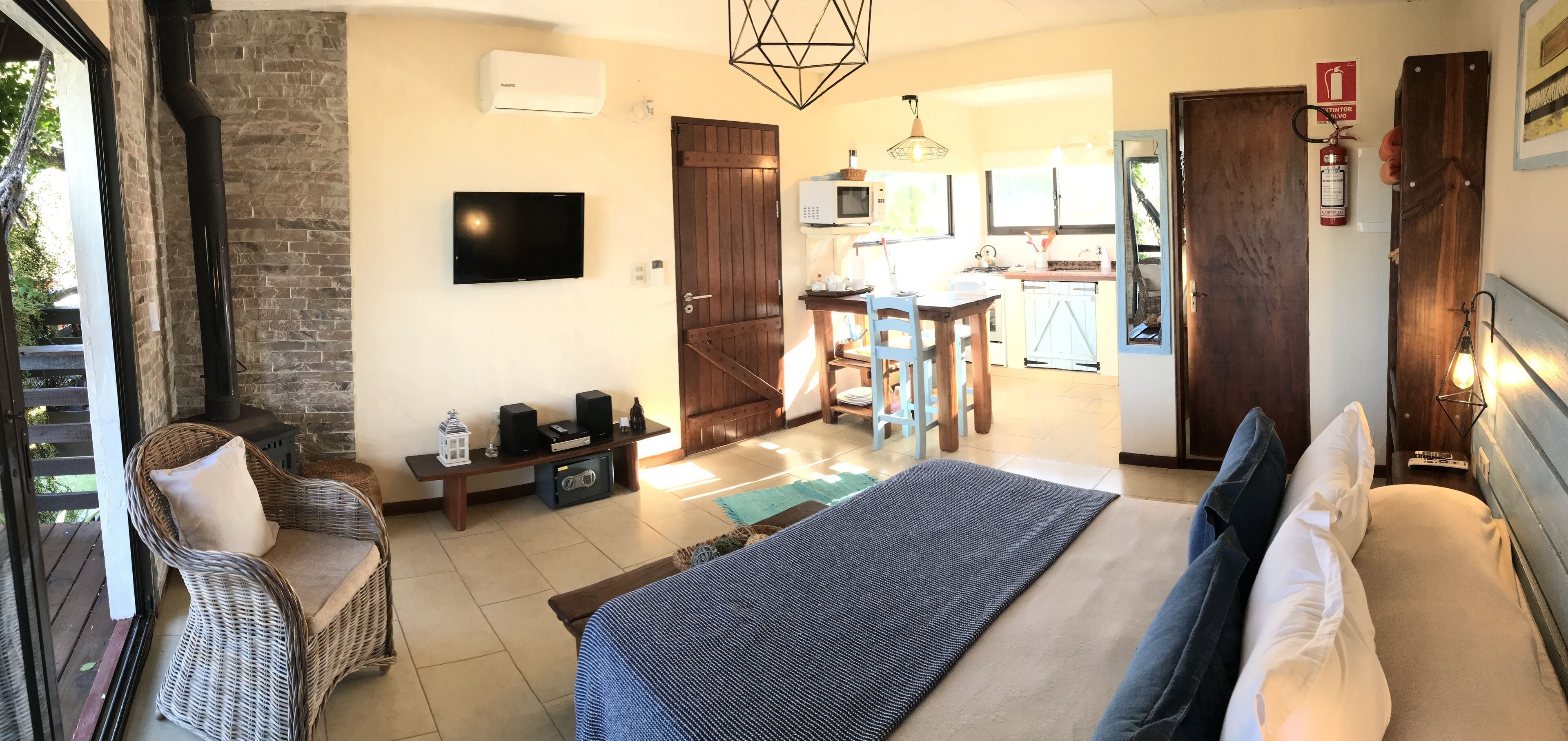 A bedroom with a large bed, a TV, a fireplace, and a view of the kitchen.
