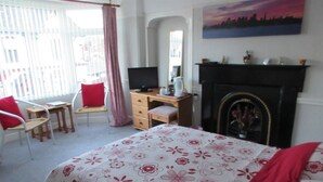 A bedroom with a bed, a desk, a chair, a fireplace, and a large window. - Ty Newydd B&B (Trefriw)