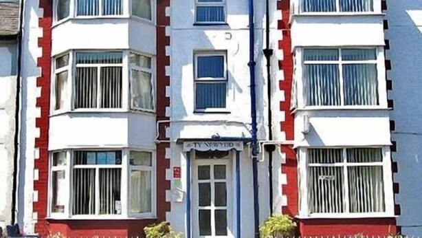 A two-story building with bay windows, a red and white facade, and a small shop sign. - Ty Newydd B&B (Trefriw)
