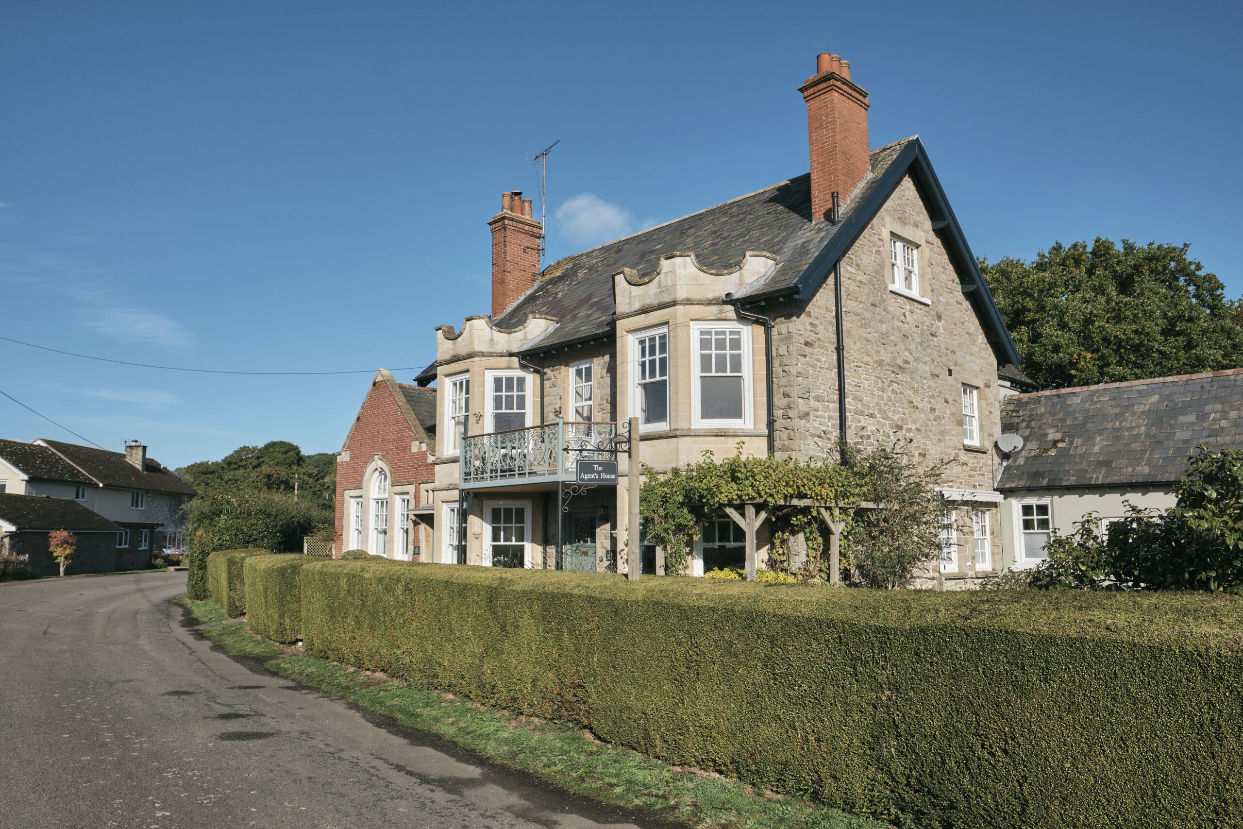 A stone building with a balcony, a sign reading "The Old Inn," and a hedge in front.