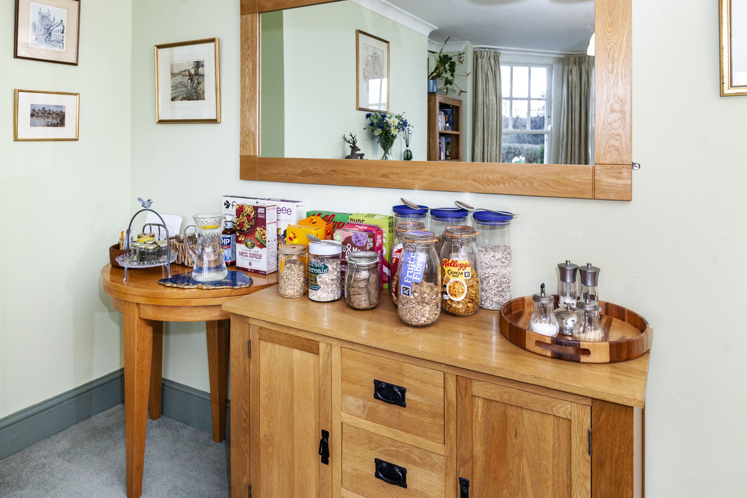 Una encimera de cocina con distintos alimentos y frascos, un mueble de madera con cajones y un espejo sobre la encimera.