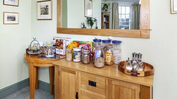 Una encimera de cocina con distintos alimentos y frascos, un mueble de madera con cajones y un espejo sobre la encimera.