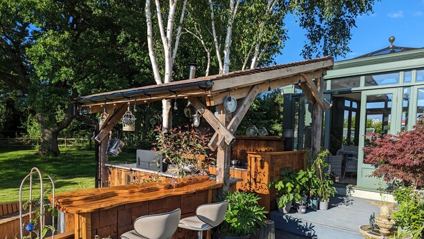 Een terras met houten meubels, een pergola en potplanten.