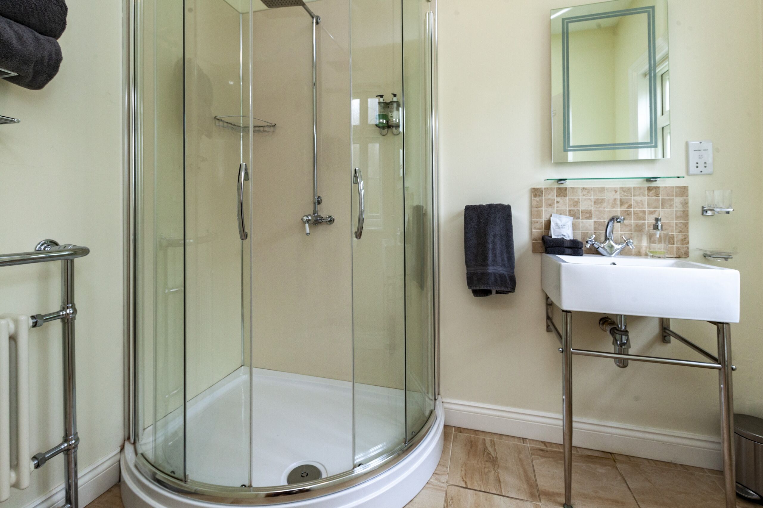 Ein modernes Badezimmer mit einer gläsernen Dusche, einem weißen Waschbecken und einem Spiegel darüber.