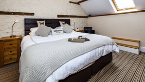 Een slaapkamer met een schuine kap, dakraam, een bed met hoofdeinde, nachtkastjes en een stoel.