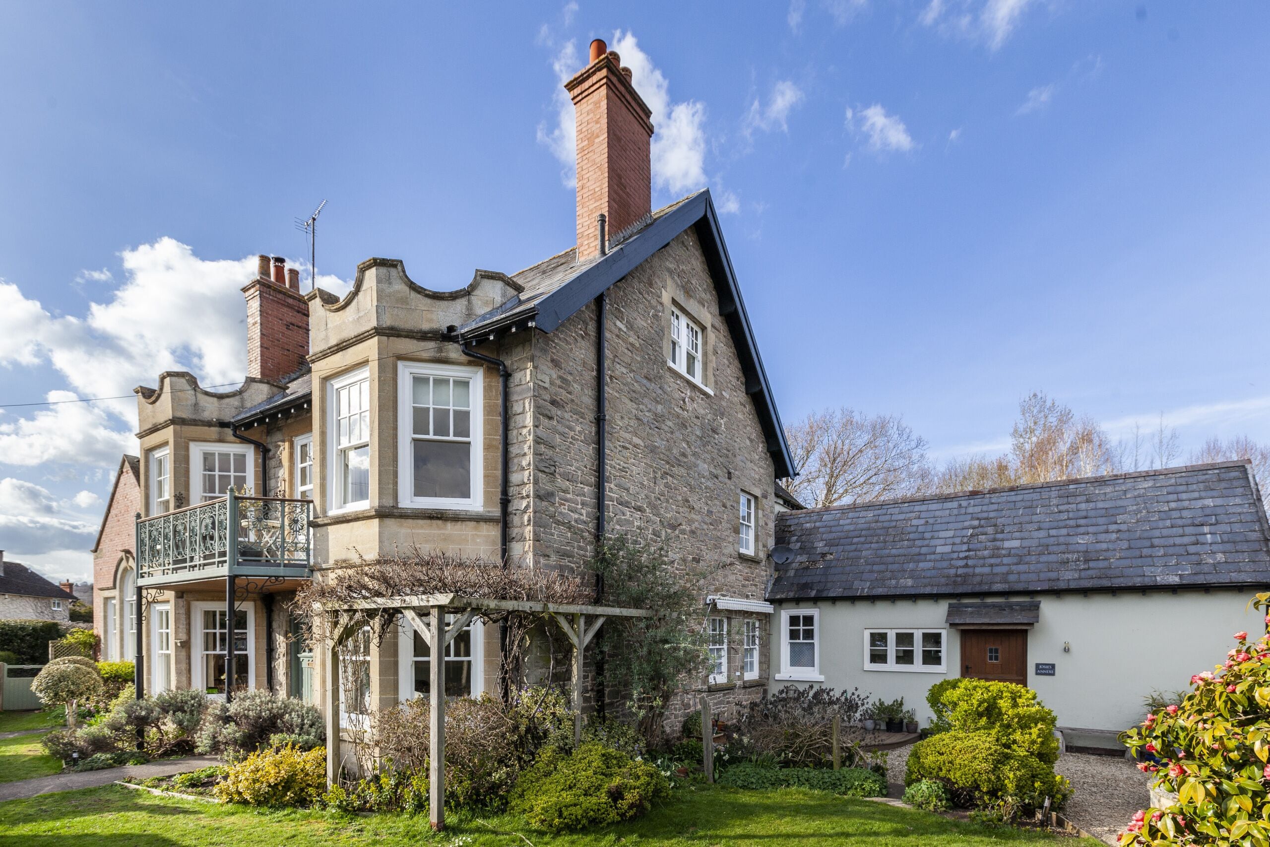 A stone building with a balcony, a garden, and a smaller attached building.