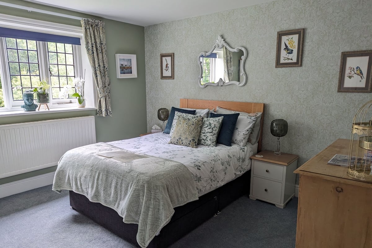Een slaapkamer met een bed, nachtkastjes, een dressoir en een raam met gordijnen.