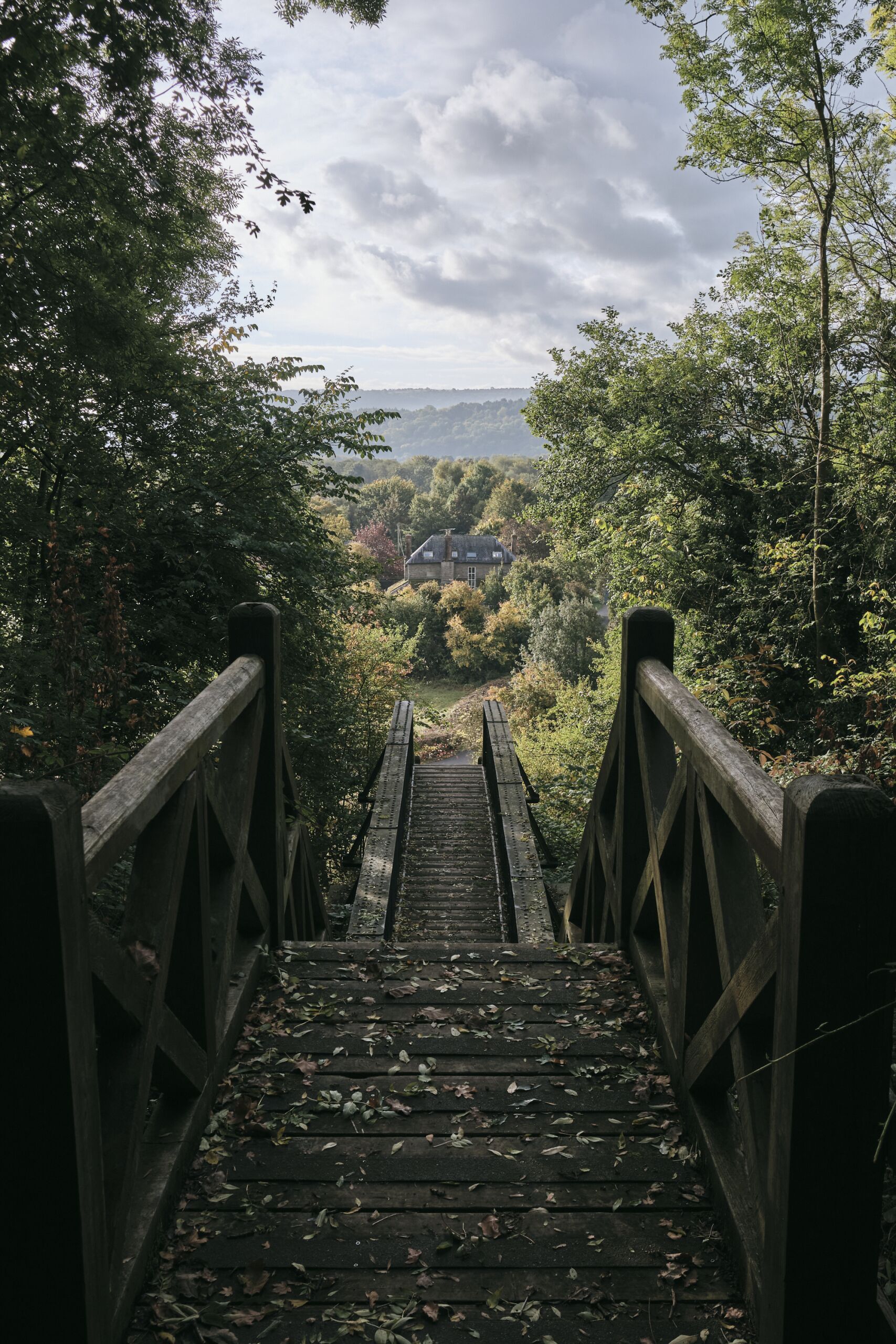 A wooden bridge leading to a house surrounded by trees.