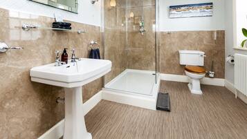 A modern bathroom with a glass-enclosed shower, a pedestal sink, and a toilet with a wooden seat.