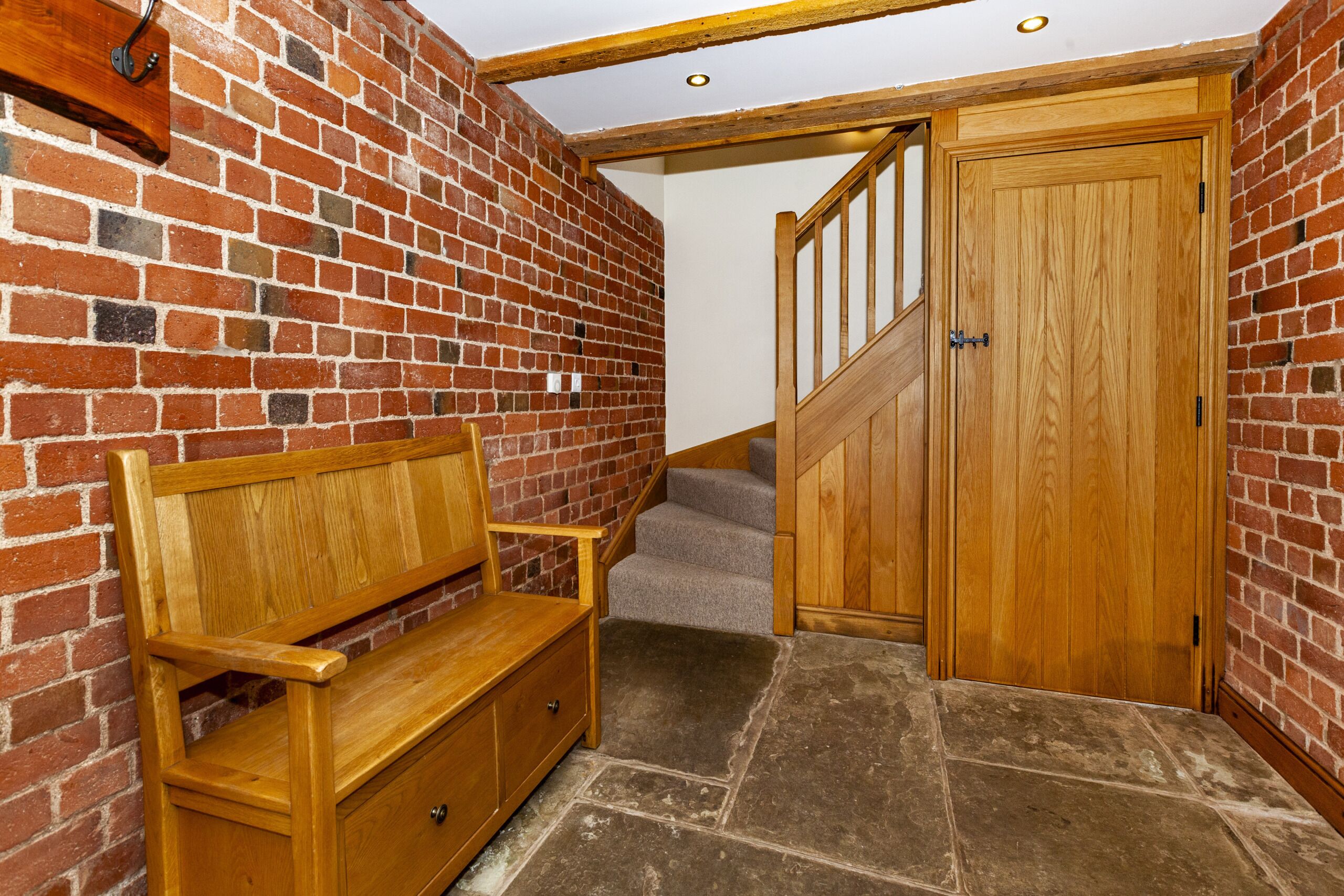 A wooden bench against a brick wall, a staircase leading to a wooden door, and stone flooring.