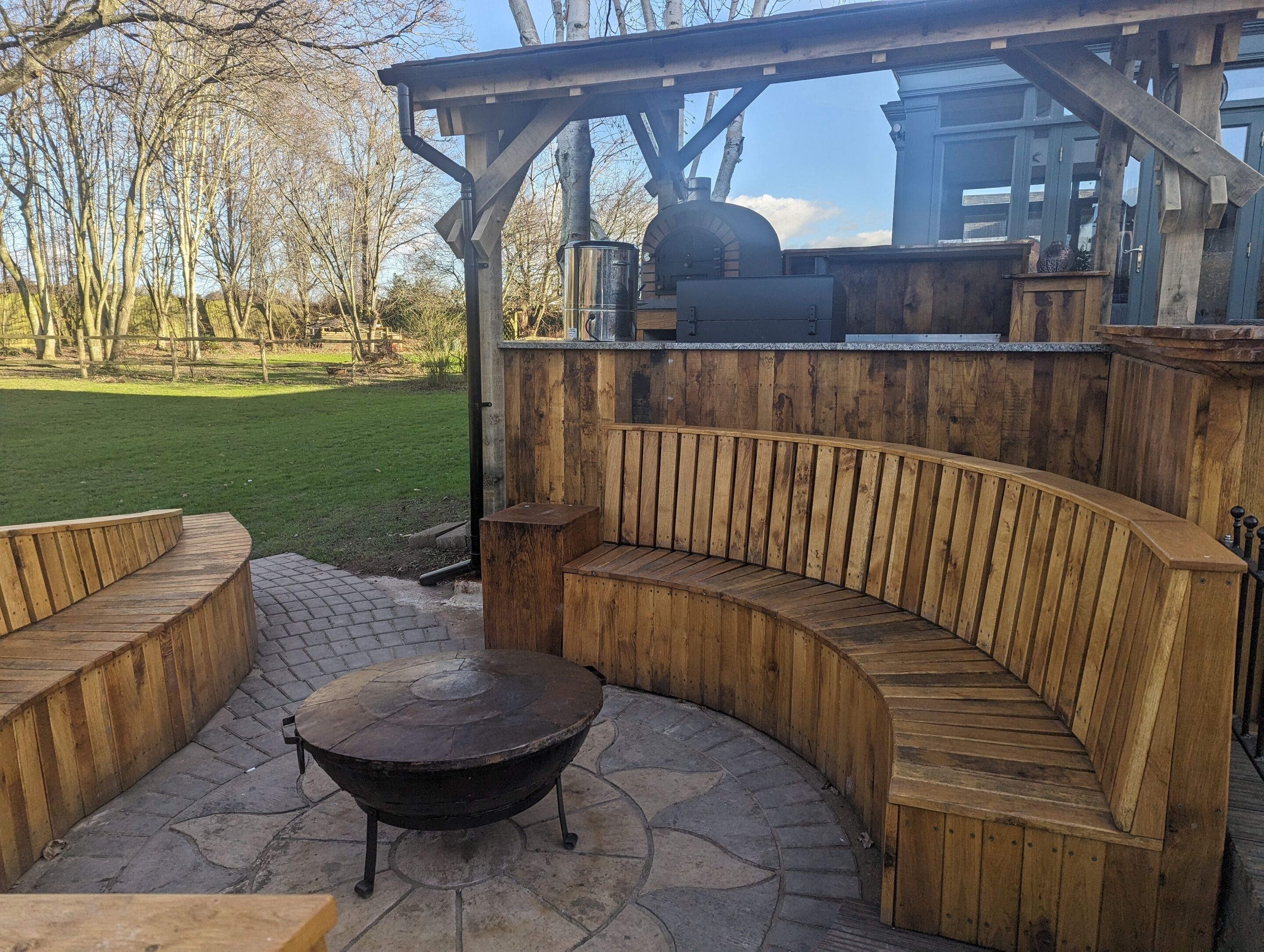 Eine hölzerne Außenlounge mit einem runden Tisch und einem Grill.
