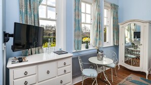Een kamer met een televisie, een witte kapstok, een ronde tafel met stoelen en een spiegelkast.