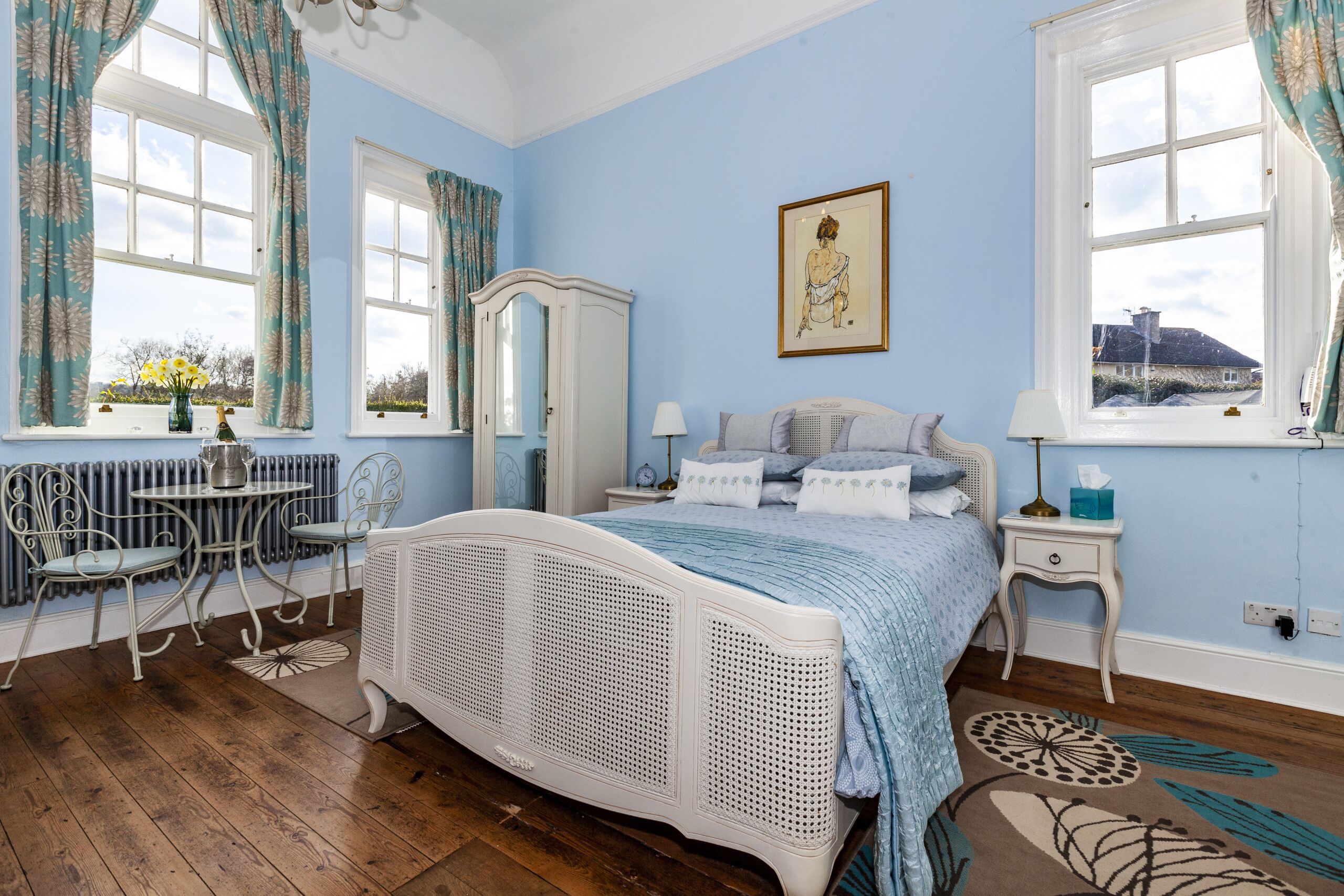 Un dormitorio con cama blanca, cómoda, silla, mesa y ventana con cortinas.