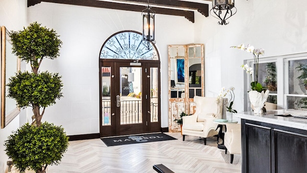 A spacious lobby with a wooden floor, a large arched doorway, and a seating area with a white sofa and a small table. - Hotel Marisol Coronado (Coronado)