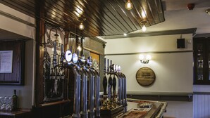 Zona de bar con varias llaves de cerveza, un dardo y una pared de madera con una placa.