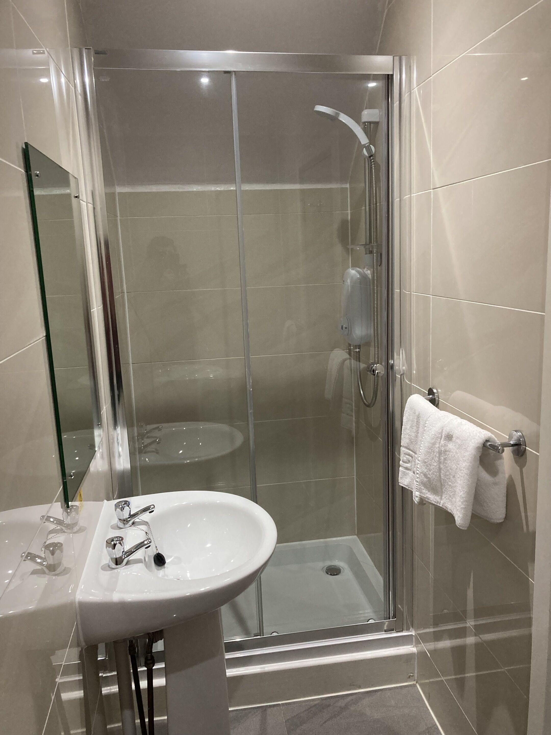 A modern bathroom with a glass-enclosed shower, a white sink, and a towel rack.