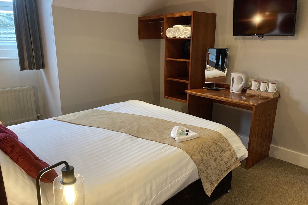 A neatly arranged hotel room with a bed, a wooden desk, a mirror, a lamp, and a coffee maker.