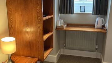 A hotel room with a wooden wardrobe, a bedside table with a lamp, a window with curtains, and a radiator.