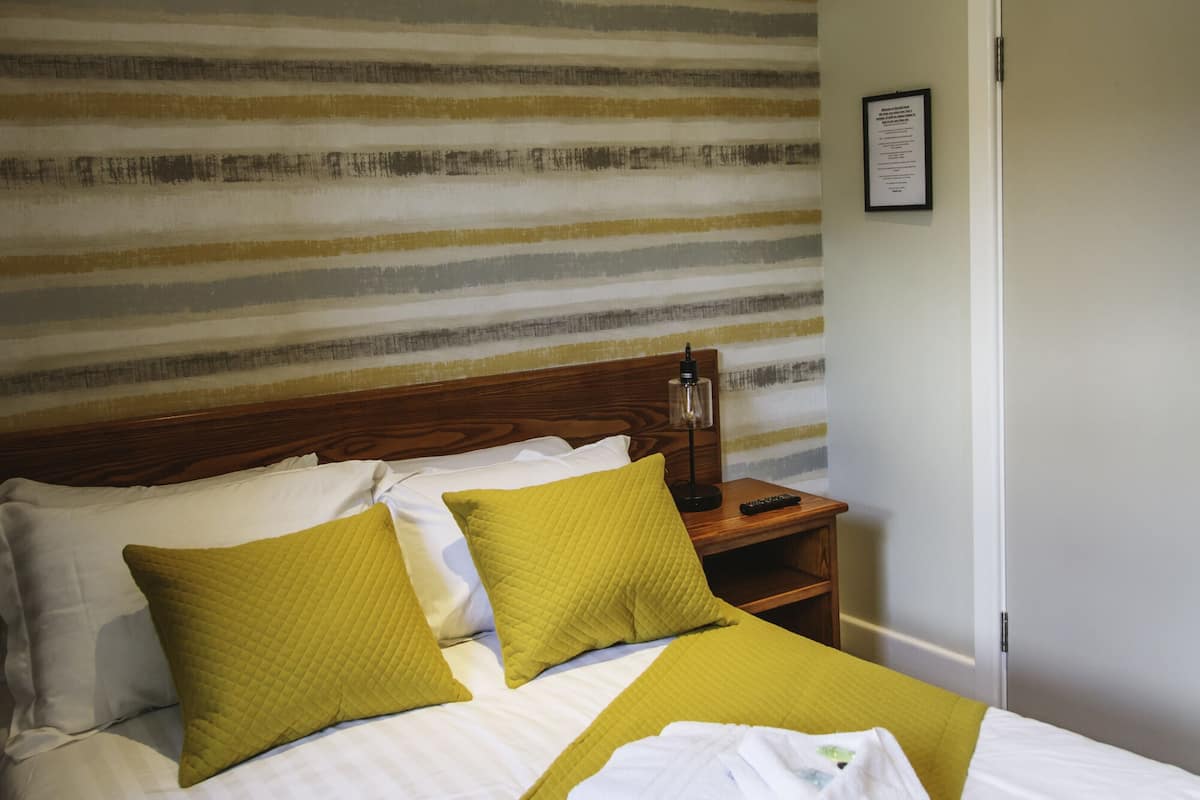 A neatly made bed with green bedding, a wooden nightstand with a lamp, and a striped wall behind the bed.
