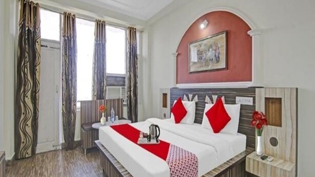 A hotel room with a large bed, a painting on the wall, and a window with curtains. - Hotel Ishan (Reasi)