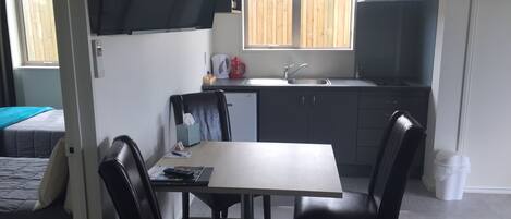 Cocina compacta con comedor, un refrigerador pequeño y ventana con vista a una cerca de madera.