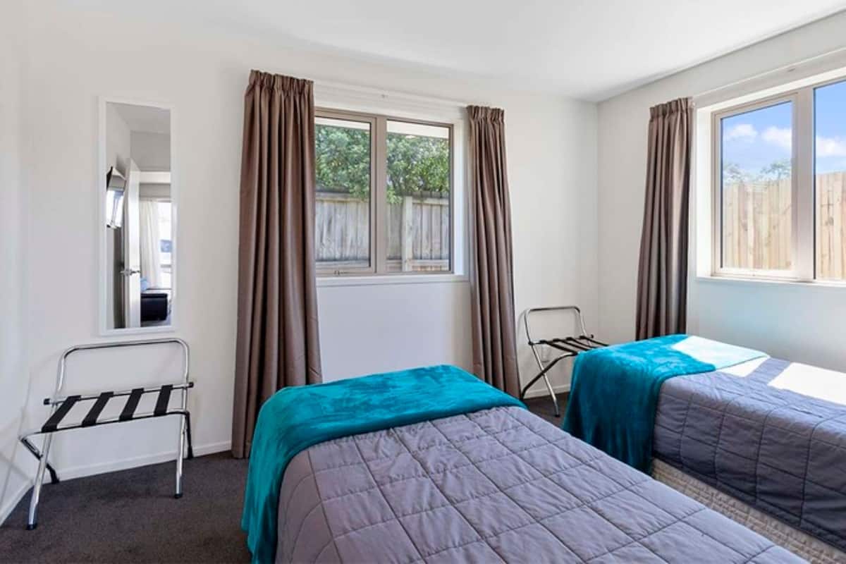 A room with two beds, a window, a mirror, and a chair.
